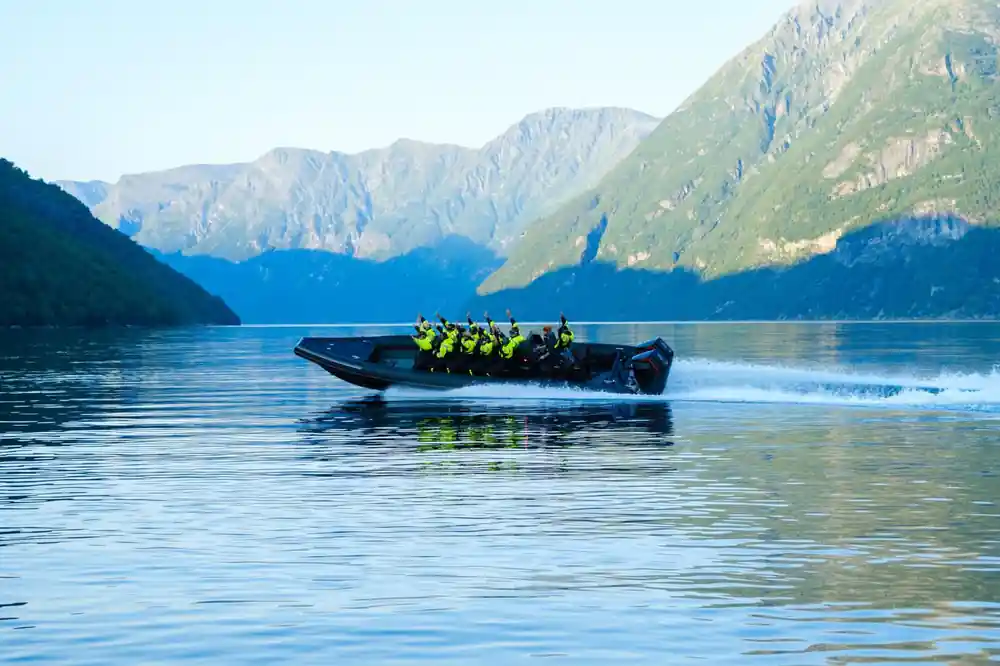Black speedboat with passengers on calm blue lake between mountains