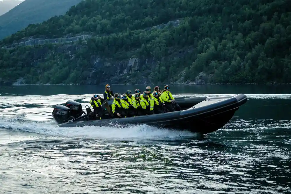 Black speedboat with passengers creating wake on dark water