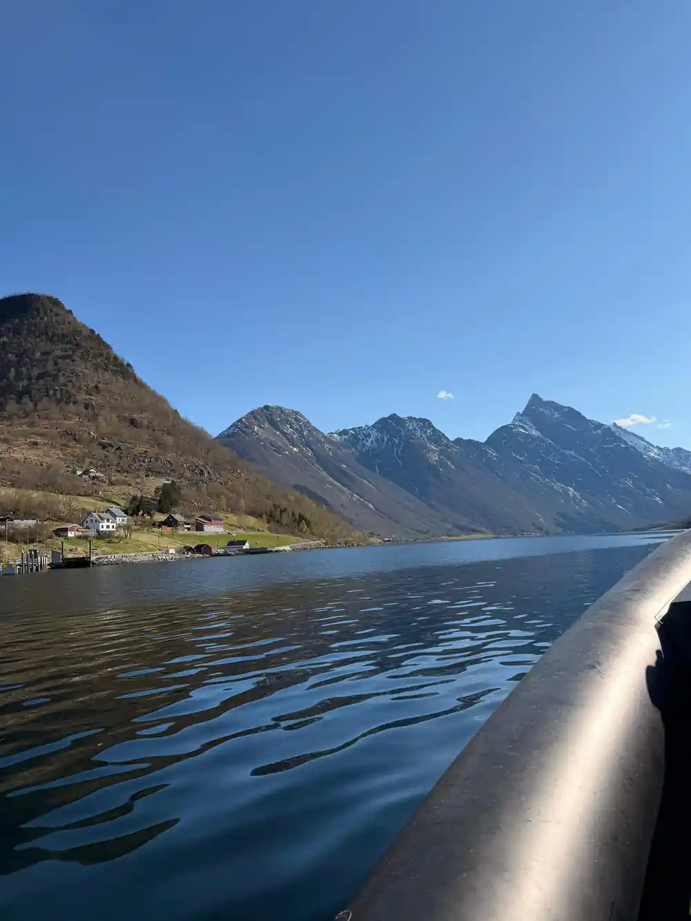 Brown mountains and small white house reflected in blue fjord