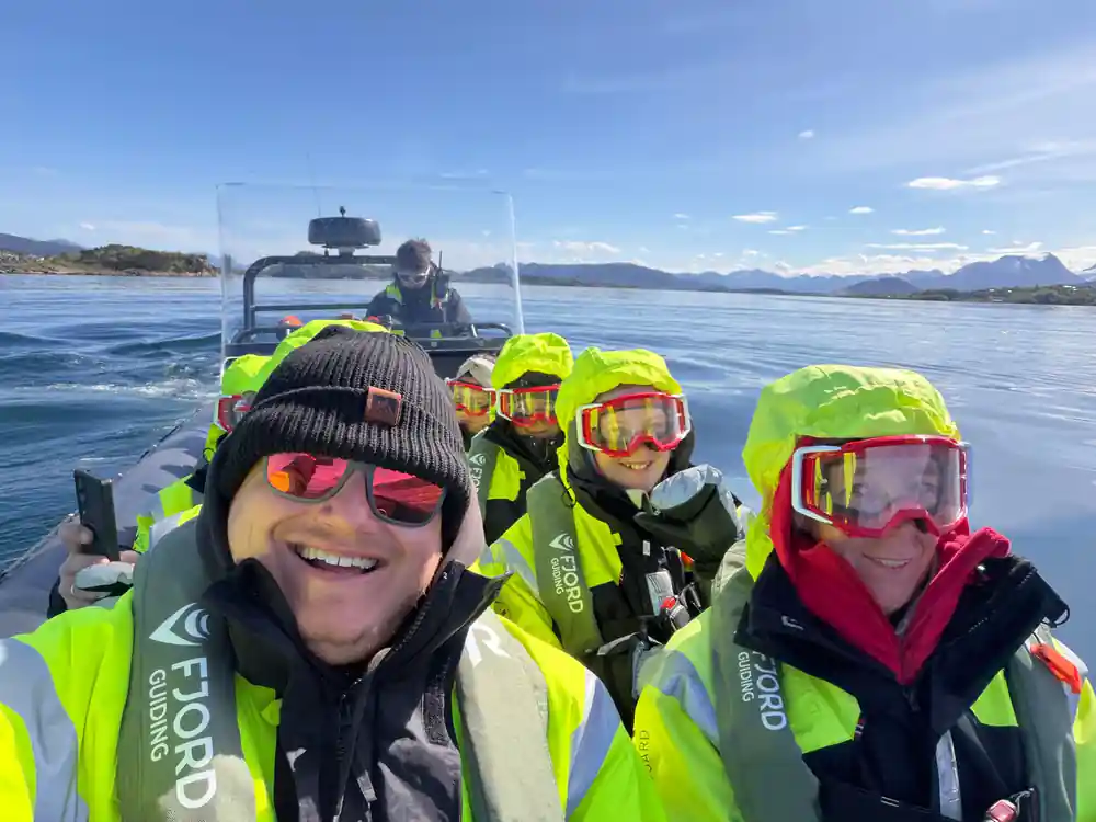 Four people in bright safety gear smiling in rigid boat