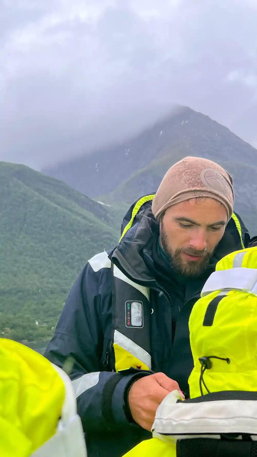 Man in yellow gear and beanie near steep green mountain