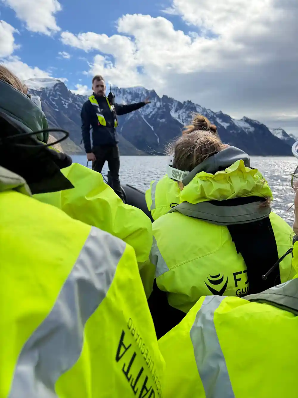 People in neon jackets on boat in snowy mountain fjord
