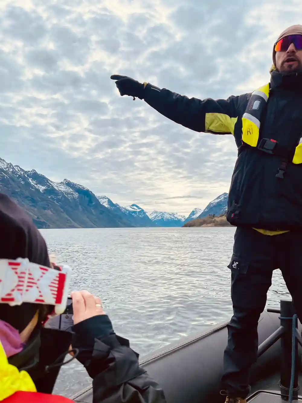 Person in life jacket pointing across mountain lake from boat