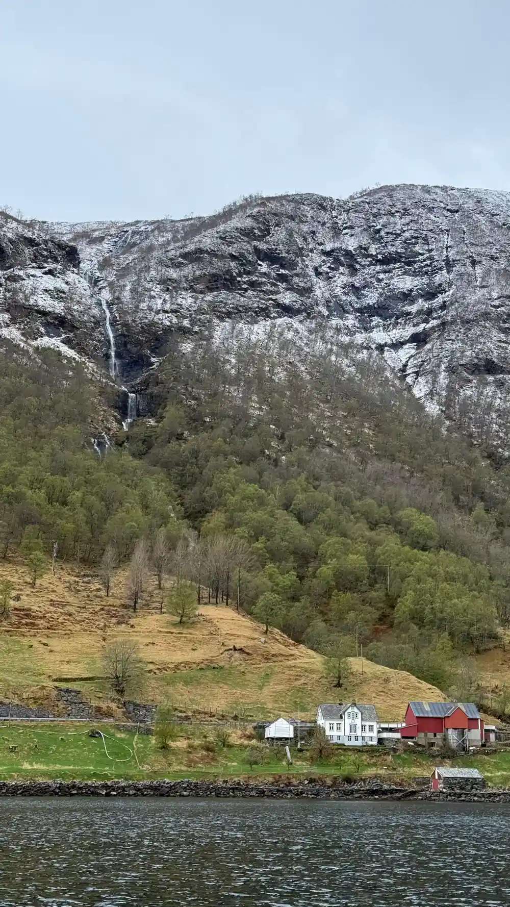 Red farmhouse on green slope with snow-capped mountain