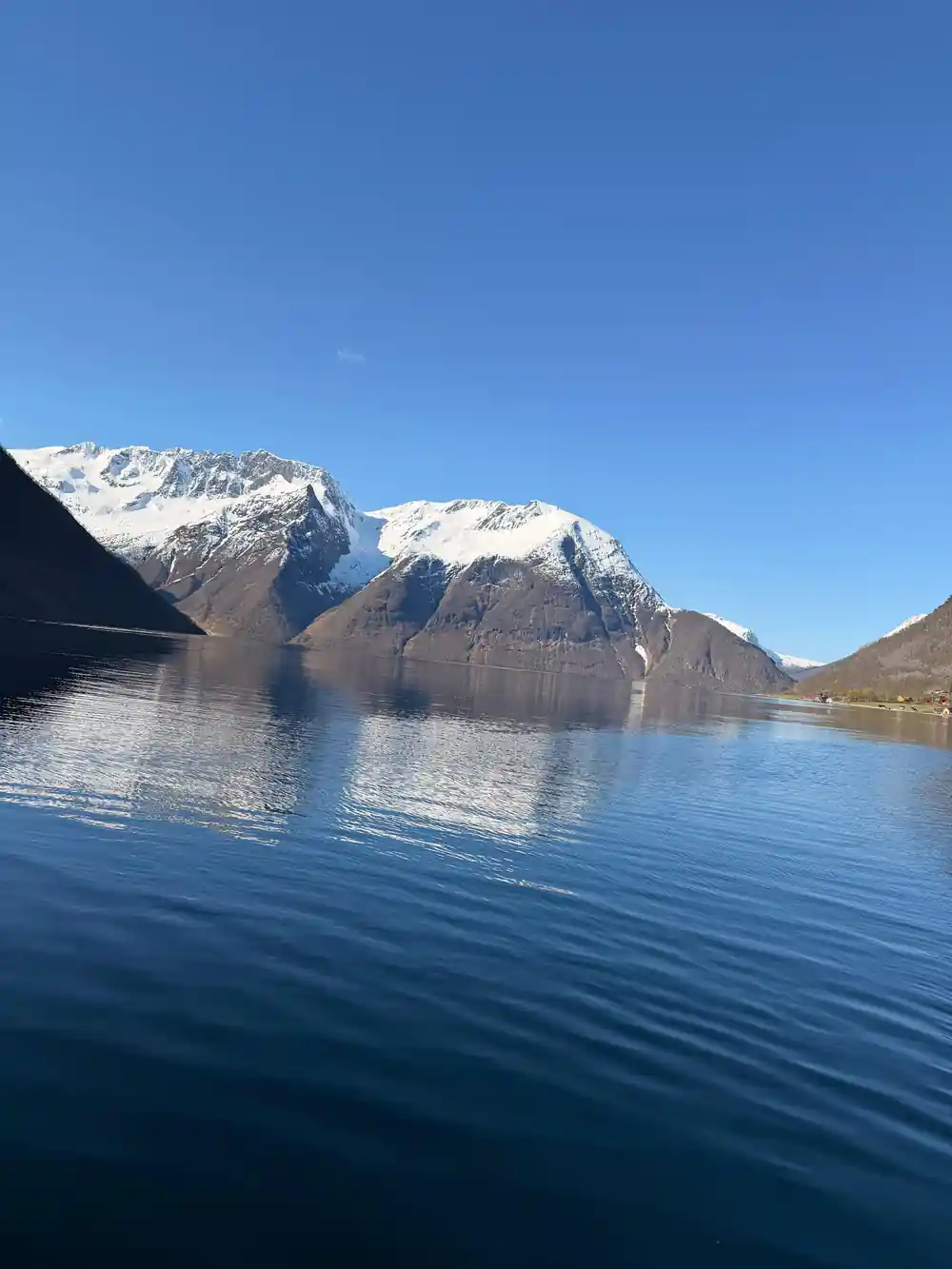 Snow-covered mountain peaks reflected in blue fjord water