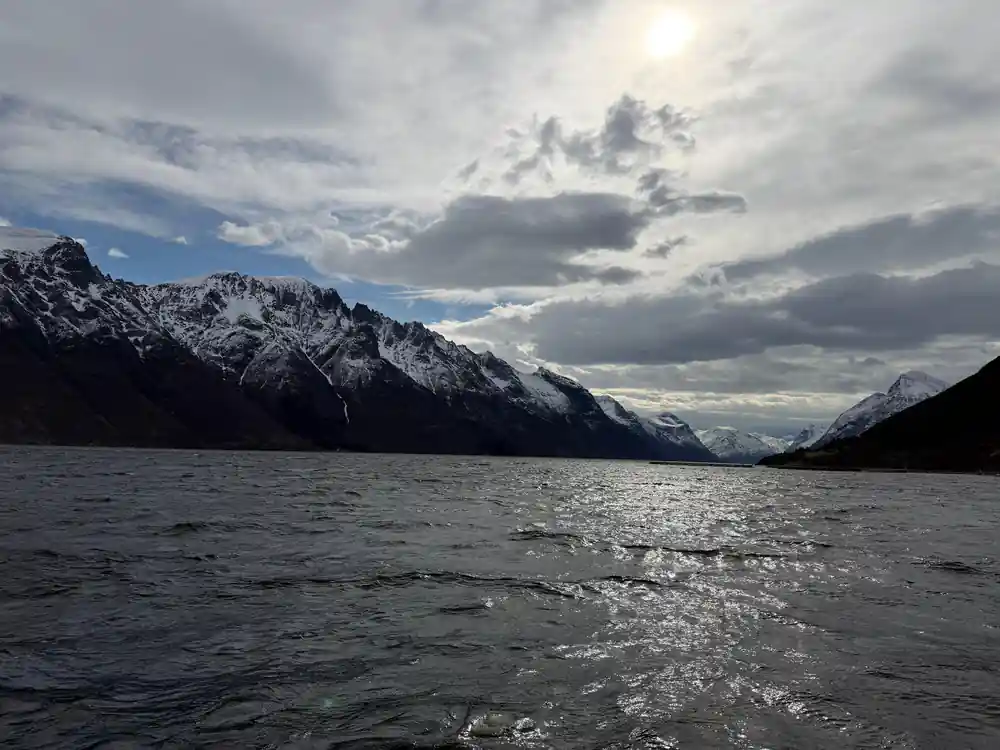 Snow-covered mountains reflected in still fjord water
