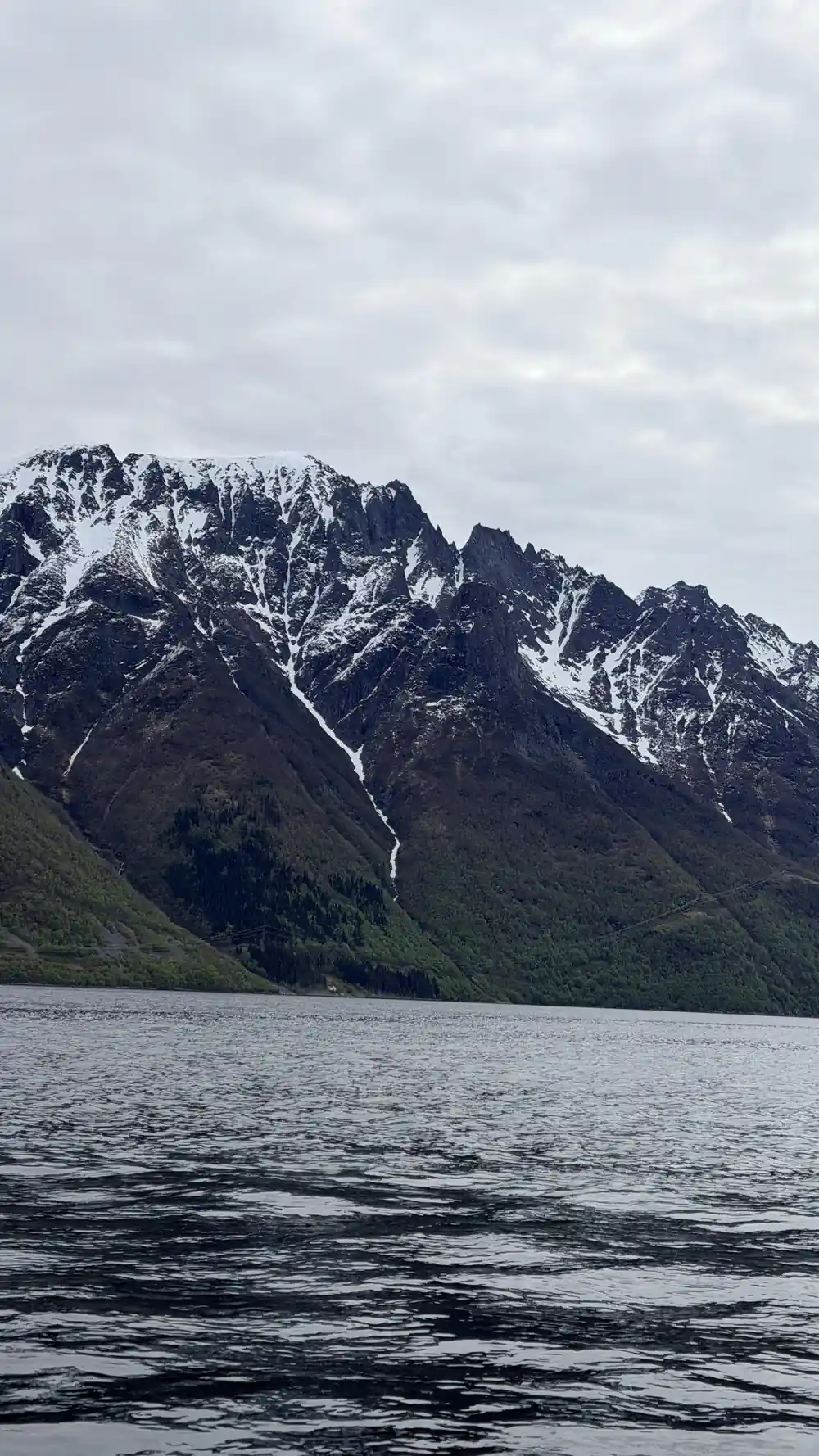 Snow and green mountain with waterfall above lake