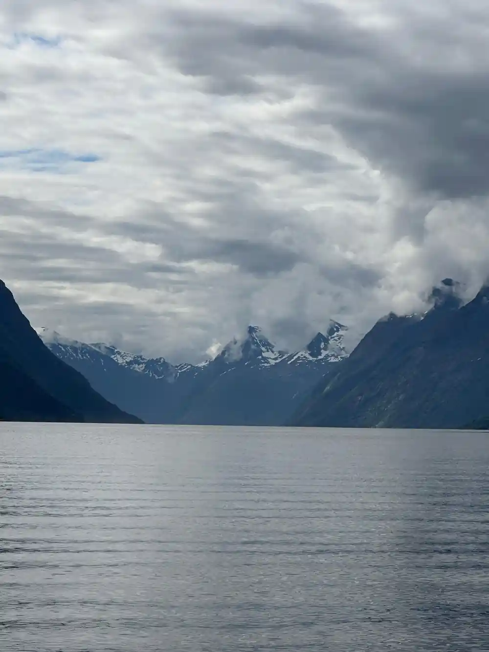 Snowy peaks and clouds above wide fjord