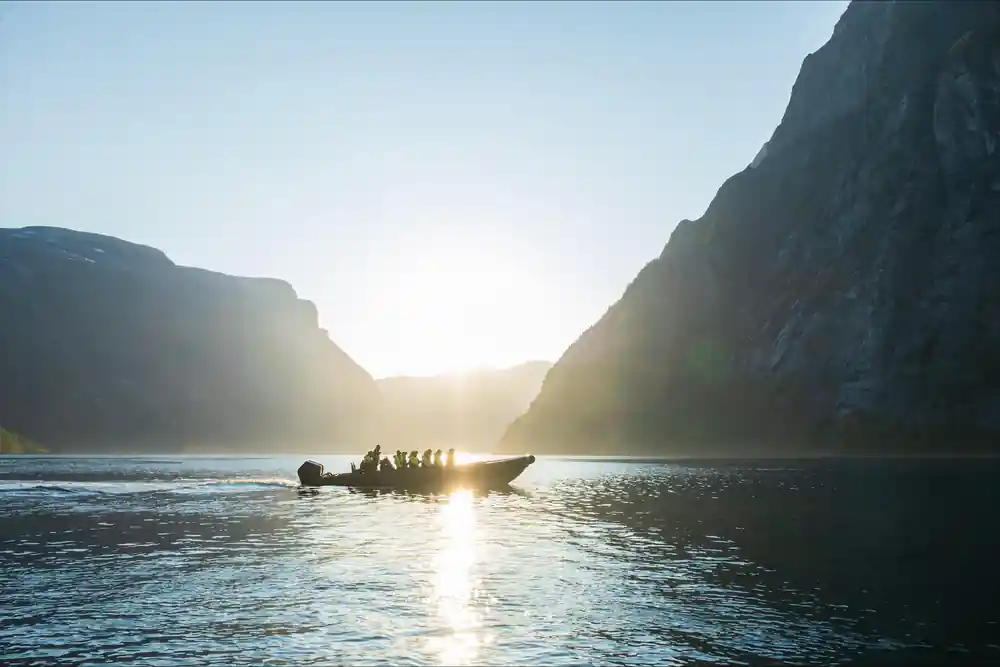 Speedboat with passengers silhouetted against mountain valley at sunset