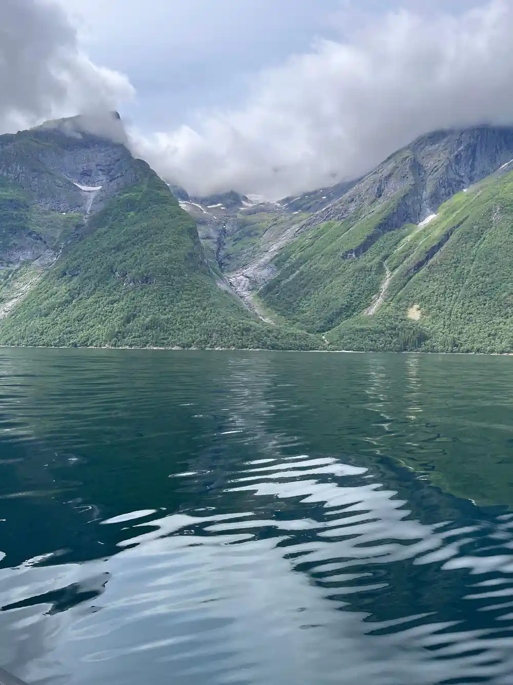 Steep green mountains with waterfalls beside fjord
