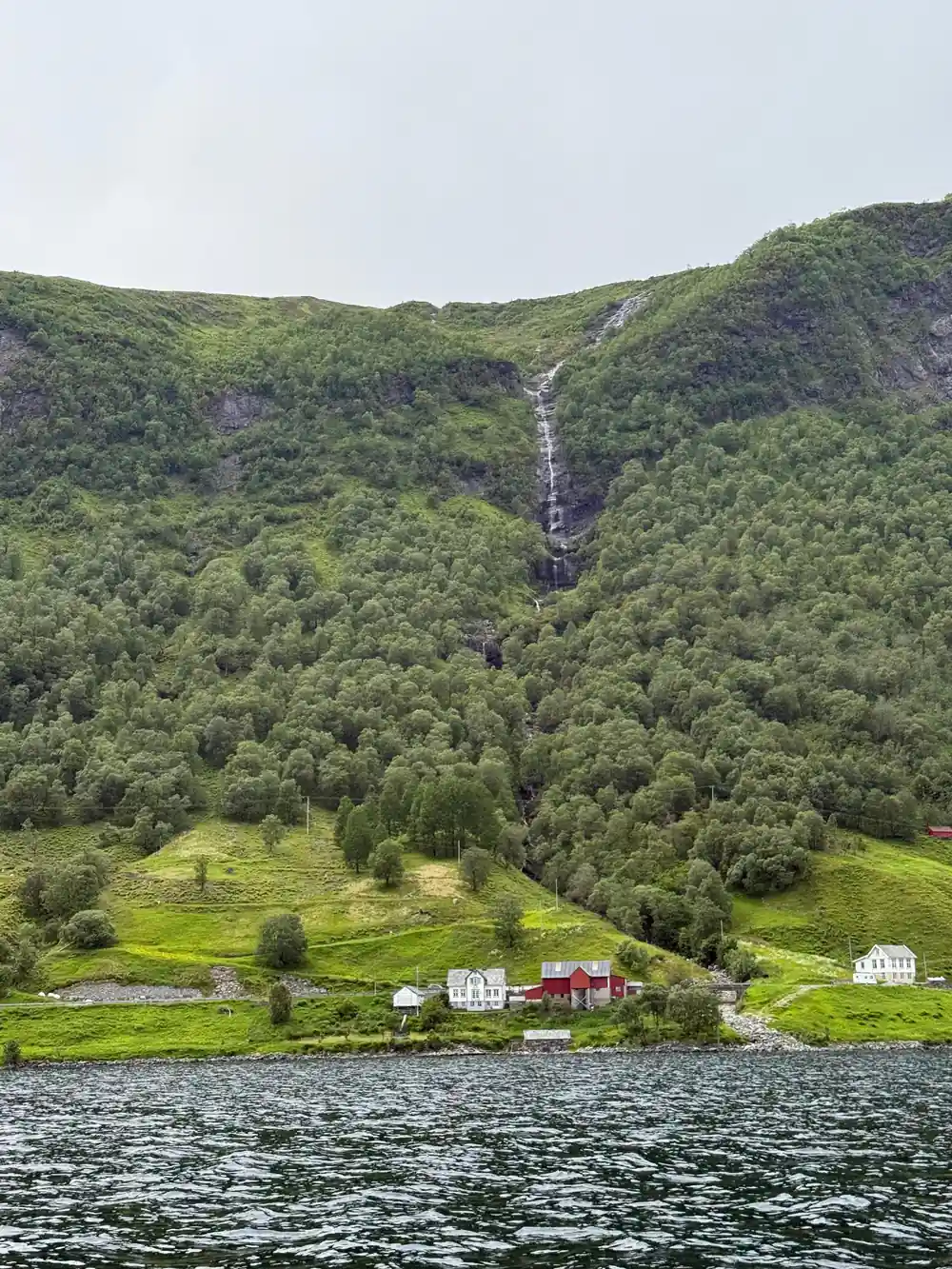 Waterfall cascading down forested mountainside above lakeside village