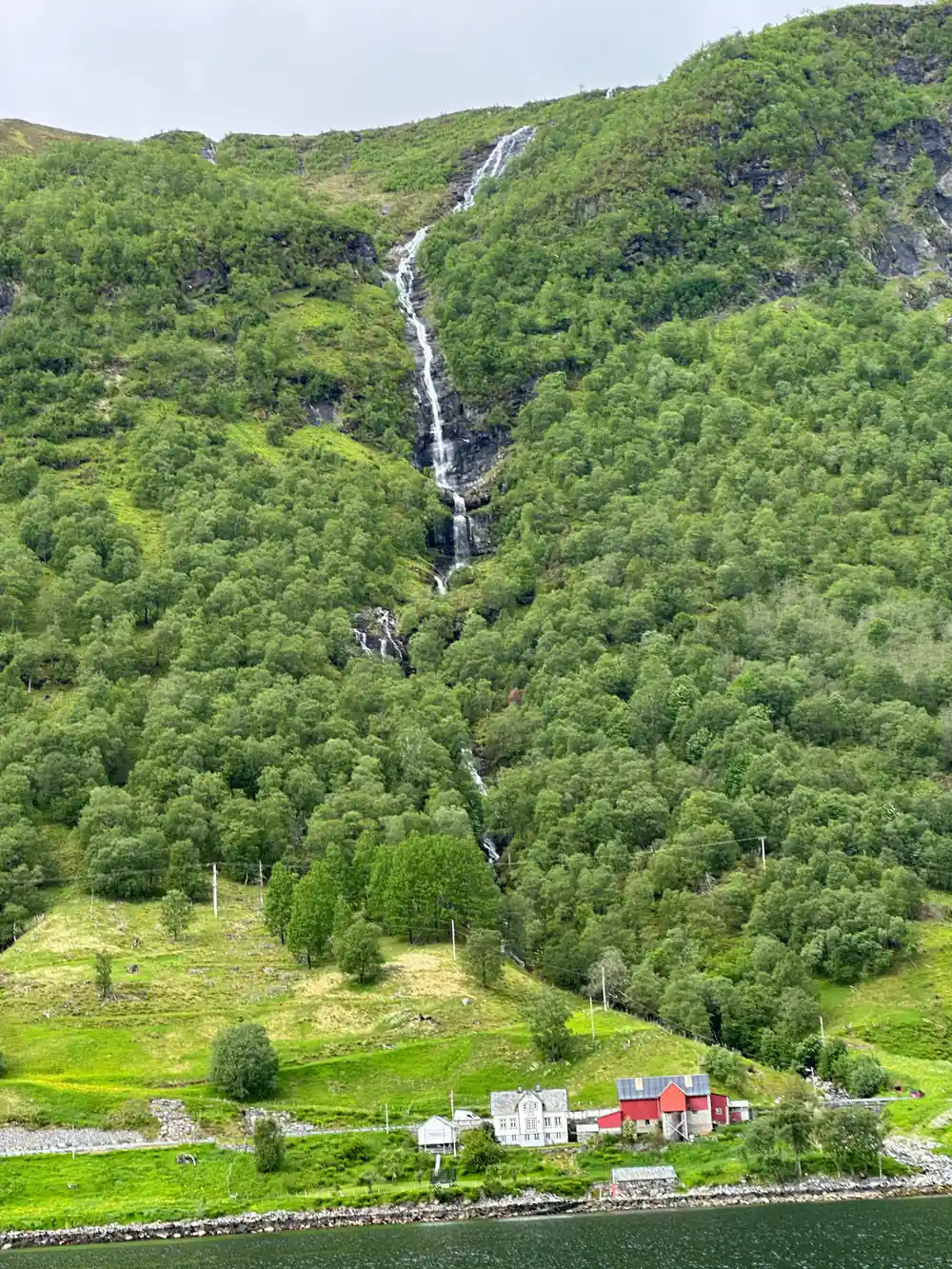 Waterfall flowing down forested mountainside near farmhouse