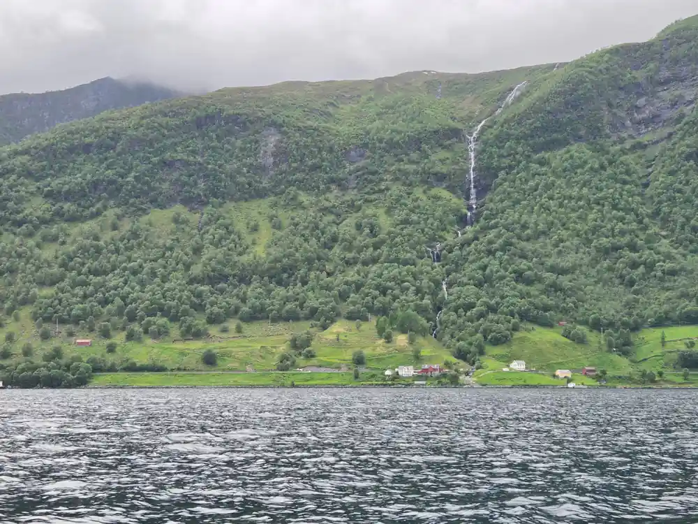 Waterfall streaming down green mountainside above water